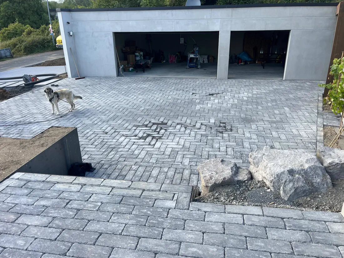 Fertige Pflasterfläche in Antikoptik vor einer weißen Doppelgarage, Findlinge als Einfassung