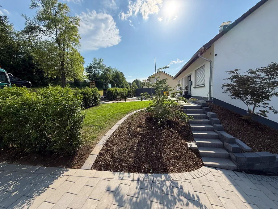 Fertige Außenanlage mit angelegter Rasenfläche, geschwungener Pflasterkante und frisch gemulchtem Beet neben einer Blockstufentreppe